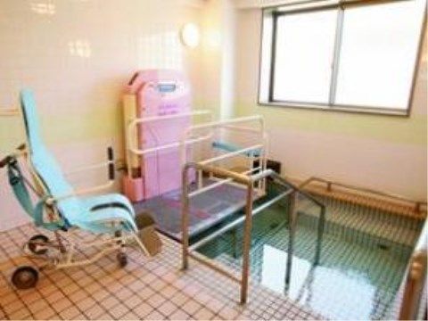 ピンクのタイルのある浴室内に、要介護の方でも入浴ができるよう、機械浴槽が設置されている。浴槽には手すりも付いている。