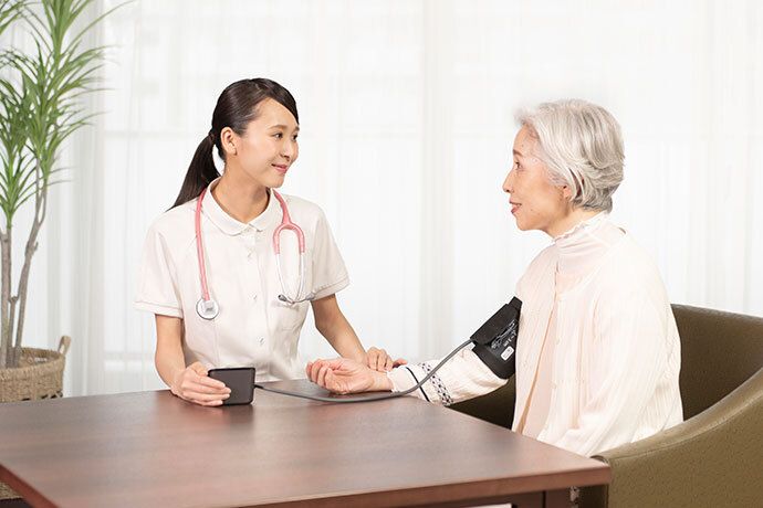 日差しが差し込む明るい居室で、男女のスタッフと話をする女性入居者様