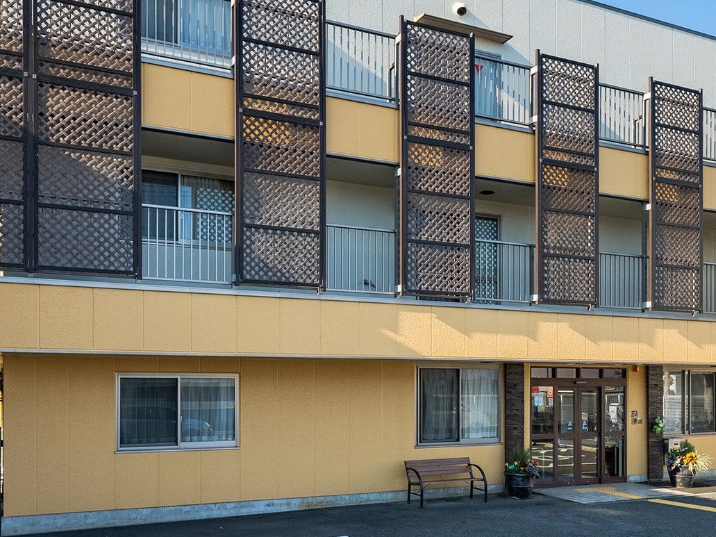 クリーム色の外観の３階建ての建物である。駐車場を完備しており、部屋と部屋の間には観葉植物が配置されている。