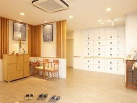 入口の横には、腰高の収納棚が置かれ、その上には花が飾られている。窓際には応接セットとテレビが置かれている。