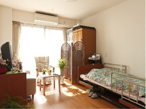 窓を背にして、１人用の椅子とカフェテーブルが置かれている。ベッドと反対側の壁には腰高の家具が置かれ、その上にはテレビがある。