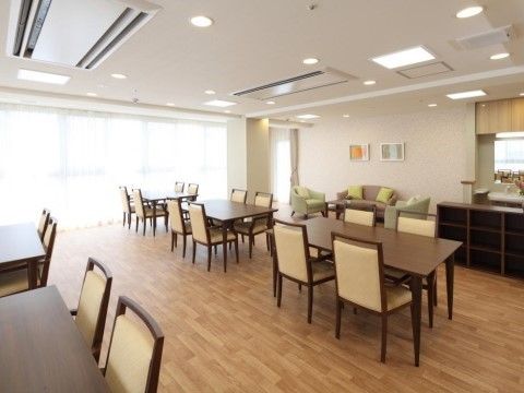 窓が壁一面に開いている。シンプルなデザインのテーブルセットが並べられ、壁際にソファセットが置かれている。