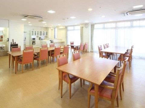 一面がほぼ窓の明るい室内に、ダイニングセットが２列間を空けて並んでいる。窓の隣には大きな食器棚と冷蔵庫がある。