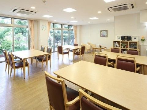 窓から庭の草木が見える明るい室内に、椅子４脚でテーブルを囲むダイニングセットが４つと、奥にソファセットが置かれている。