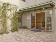 玄関はガラスの自動扉で、入り口横に施設名が表示されている。玄関マットが敷かれている。壁に沿って、植物が這っている。