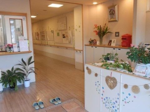 観葉植物や花がたくさん飾られ、華やかで温かみのある雰囲気の玄関である。通路には手すりが設置されている。