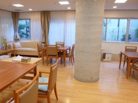 広いリビングの中央には丸い柱があり、その周辺に木製のテーブルセットが配置されている。窓辺にはソファーも置かれ、明るくてくつろげる空間である。