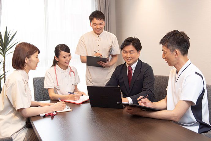 椅子に腰掛ける女性の入居者様に合わせて体勢を低くし服薬指導を行う女性医療従事者
