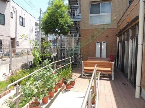 ベンチが対面する形で置かれている。スロープの両側に手すりが設置されている。手すりの足元にはいくつもの植木鉢がある。