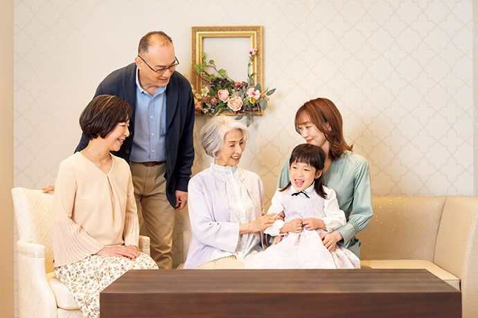 椅子に腰掛ける高齢のご夫婦に合わせ姿勢を低くし、笑顔で対応する男性スタッフ