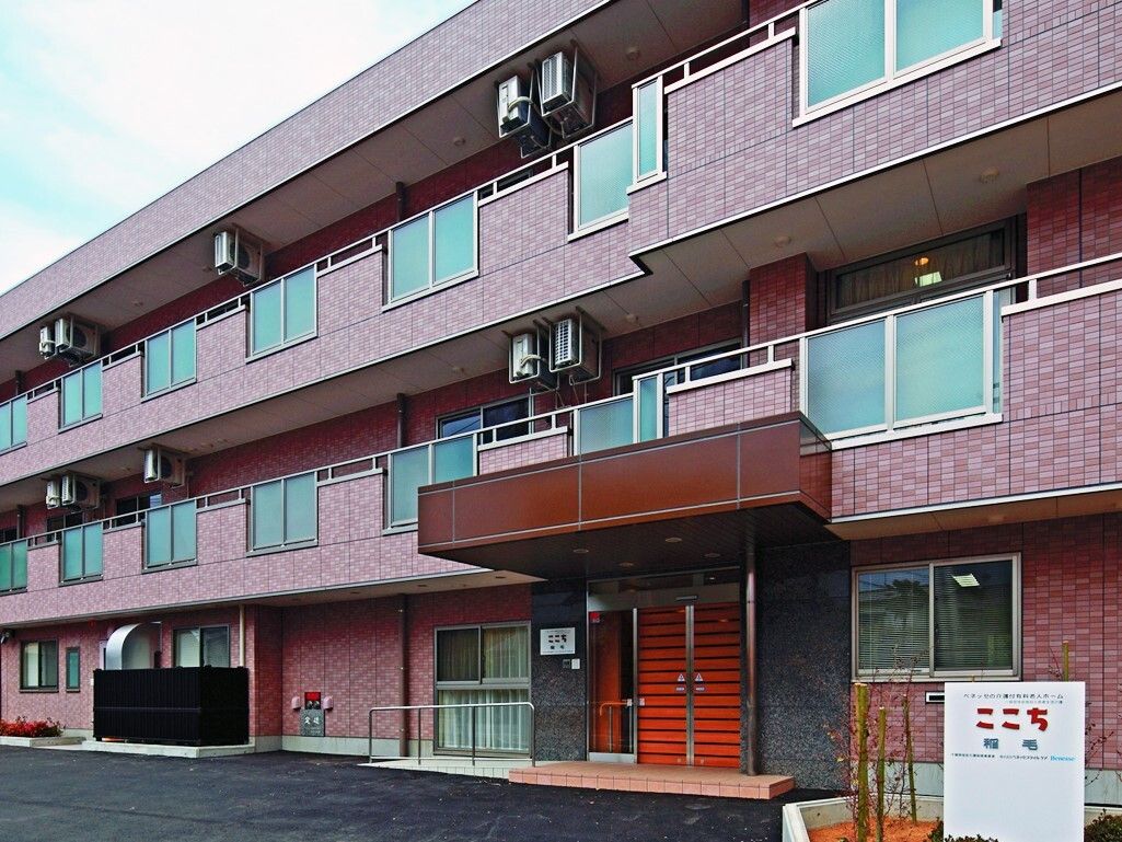 施設の建物は３階建てで、壁の色は茶色系である。部屋にはベランダが設置され、玄関には屋根が設けられている。