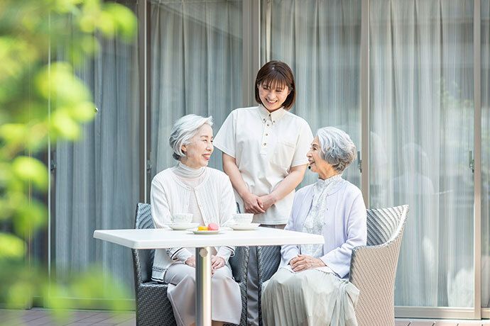 ご夫婦の入居者様がテーブル席に着き、女性スタッフの指導で書き物をしているシーン