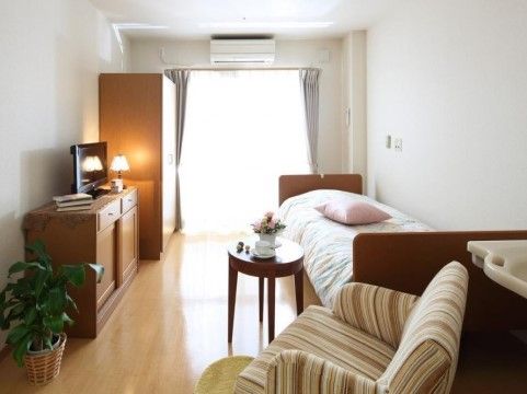 ベッド、クローゼットなどが設置されている。チェストの上にテレビが置かれている。窓の上部にエアコンが付いている。