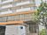 白い外壁のマンションのような縦に大きい建物である。周囲には街灯が設置され、木が植えられている。２階部分は窓がたくさんある。
