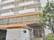 白い外壁のマンションのような縦に大きい建物である。周囲には街灯が設置され、木が植えられている。２階部分は窓がたくさんある。