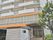 白い外壁のマンションのような縦に大きい建物である。周囲には街灯が設置され、木が植えられている。２階部分は窓がたくさんある。