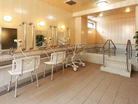 壁に備え付けられたシャワーの前に椅子が３つ置かれている。１つはキャスター付である。シャワーの左右にはステンレス製の手すりが設置されている。