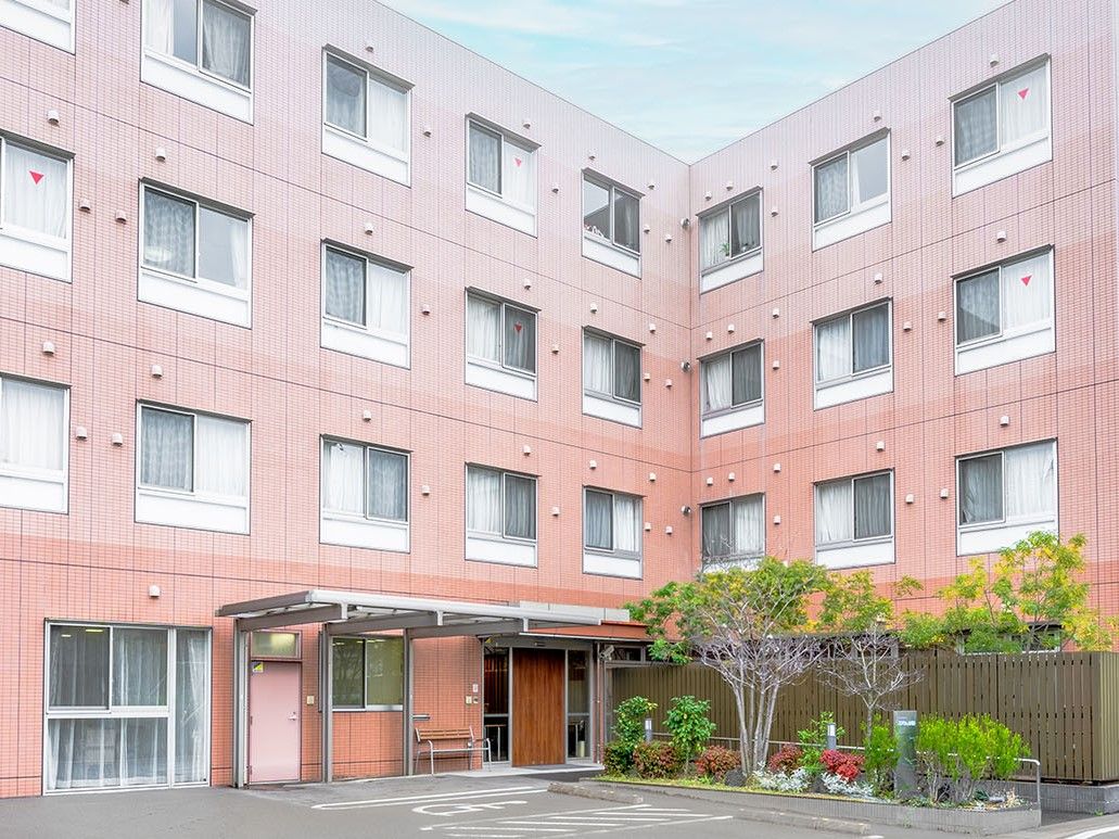 優しいブラウンの外壁で、Ｌ字型の４階建ての施設の外観。エントランスには屋根が設けられ、車から雨に濡れずに施設に入ることができる。