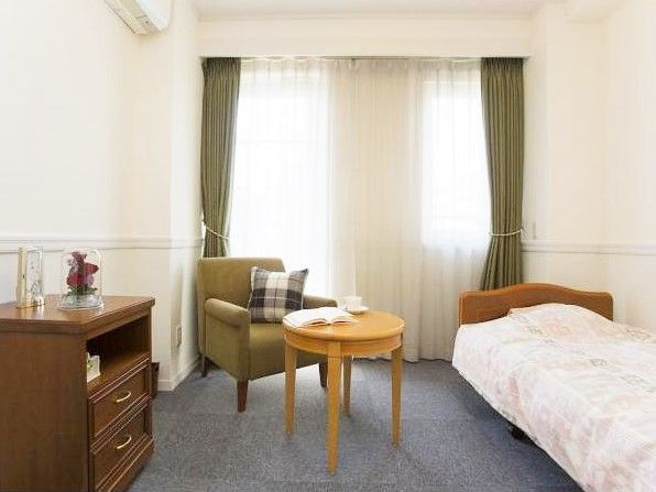 低めのベッドや一人掛けのソファー、木目の小さな棚のある部屋