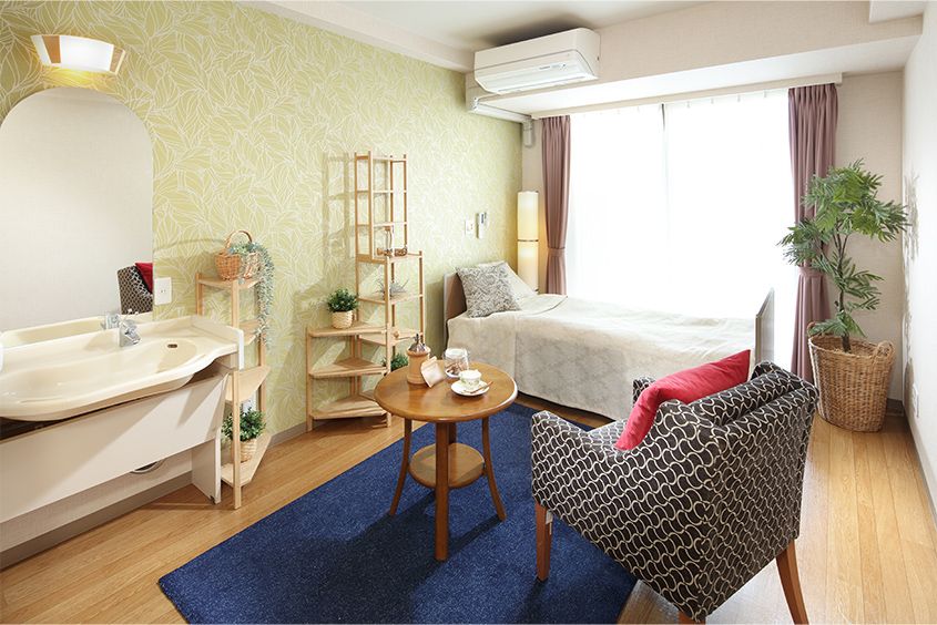 ベッドのシーツが少し乱れているなど、生活感のある部屋。中央にある丸テーブルの上にはコーヒーカップと花が置かれている。