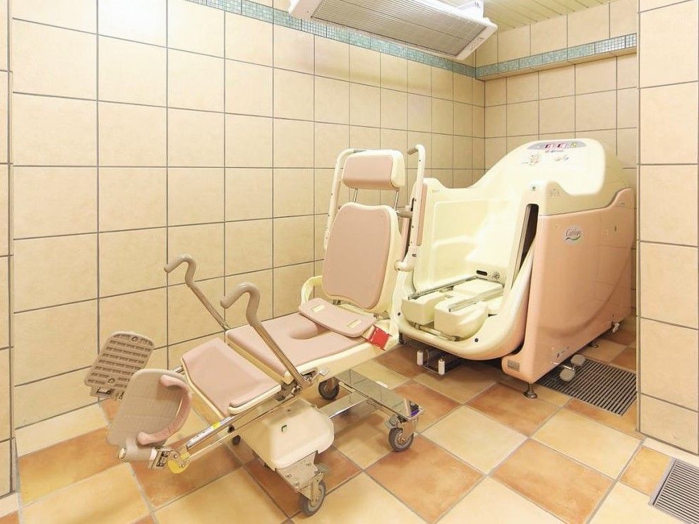 茶色とベージュのタイルが敷かれている、座位入浴用のストレッチャーが置かれた浴室