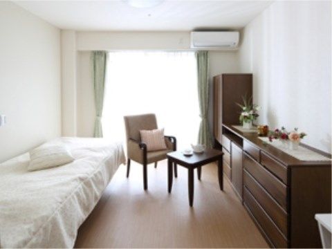 白い壁に茶色の家具がモダンな雰囲気の居室。ベッドと家具の間に一人掛けのソファとテーブルが置かれている。