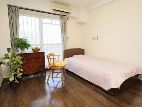 落ち着いた色合いのフローリングの上には、ベッドと腰高の引き出しタンス、白木風の椅子が置かれている。部屋に置かれたグリーンが目に優しい。
