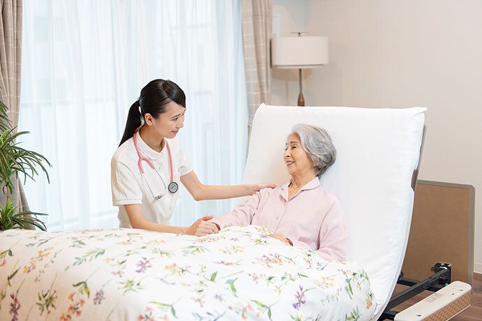 施設の職員により血圧測定を受けているベッドに横たわった女性