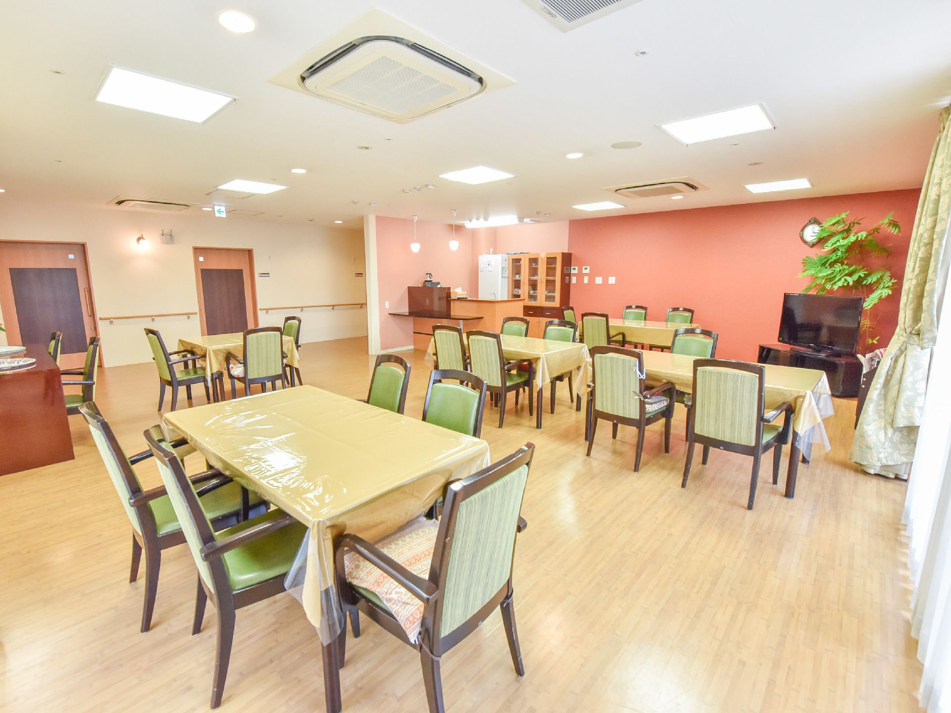 5台の机が置かれている。それらにかかっているテーブルクロスは全てクリーム色で椅子は座る部分と背もたれの部分が緑色で他は木材でできている。