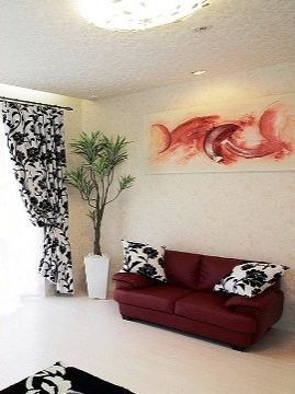 壁際には深紅のソファーが置かれ、ソファーの上の白い壁には抽象画のような絵画が飾られている。窓際には大きな観葉植物が置かれている。