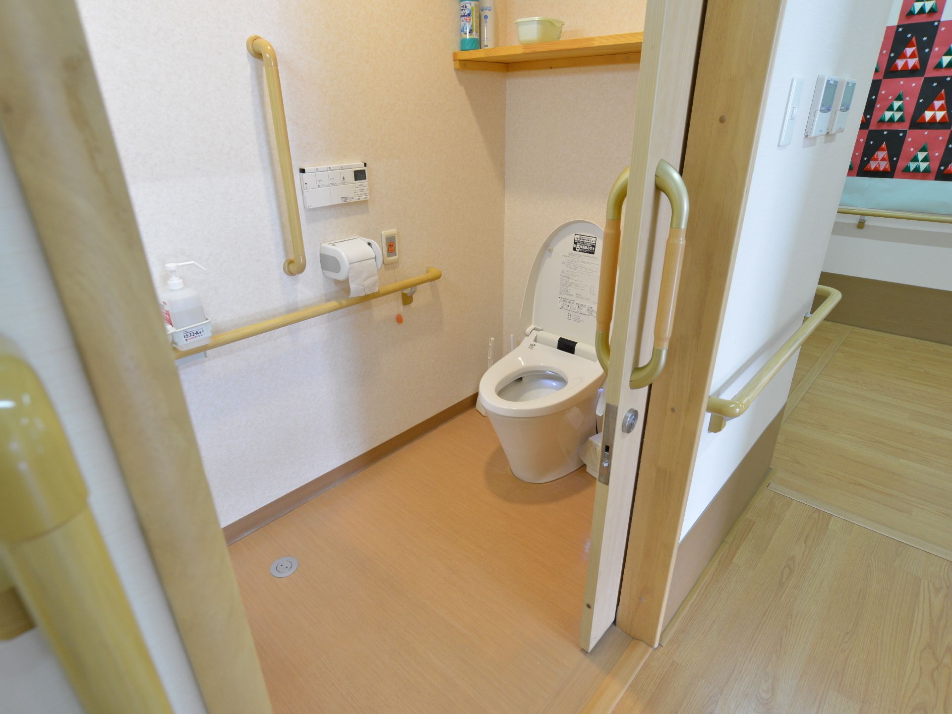 トイレ内には縦型と横型の手すりが取り付けられている。壁側にはトイレットペーパーフォルダーが1つとナースコールボタンが設置されている。