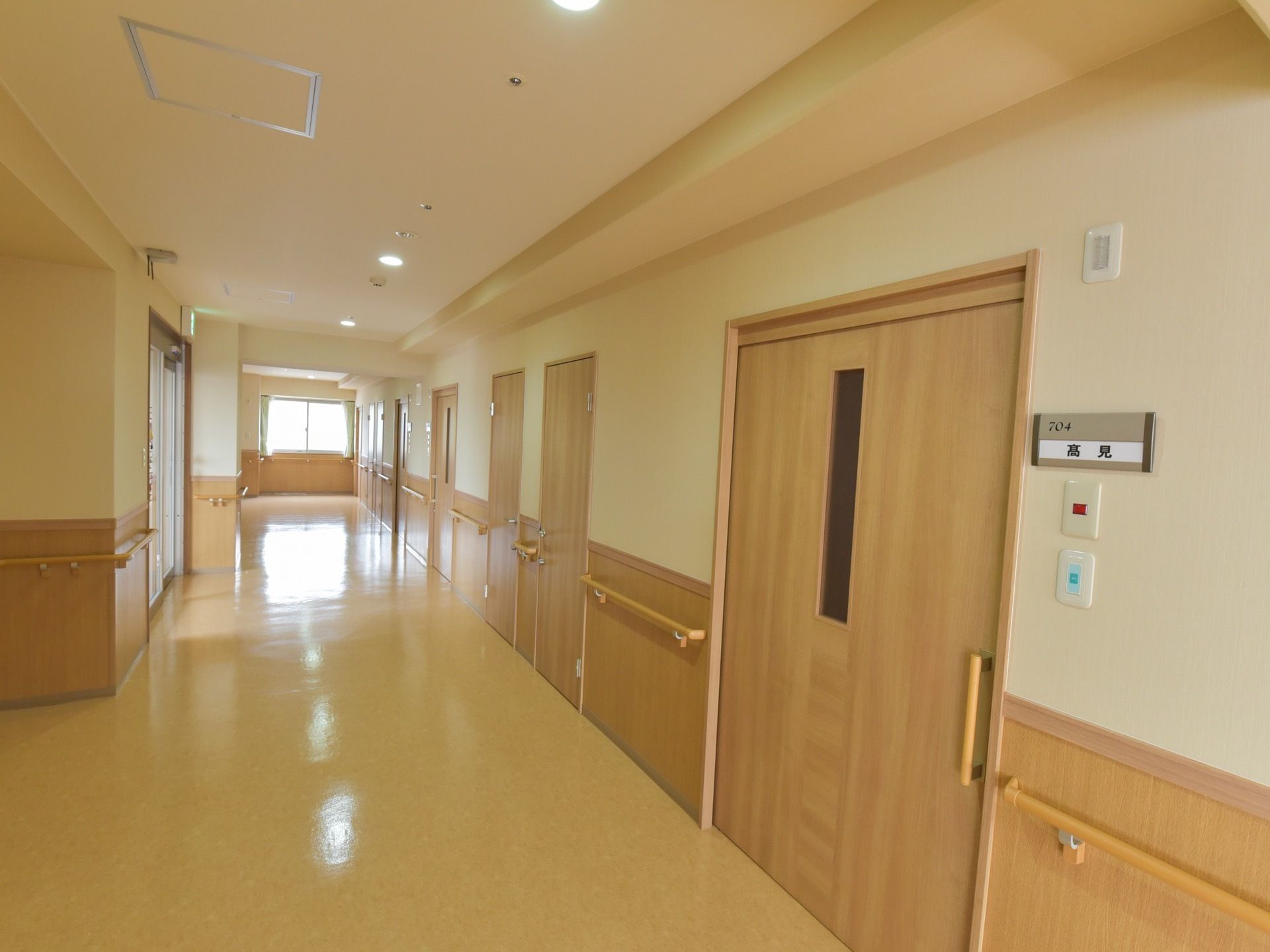 通路の壁には手すりが設置されていて、部屋の扉が並んでいる。入居者様の居室前には部屋番号と名前を貼っている。