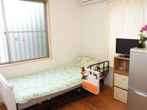 介護用ベッド、冷蔵庫、棚の上に置かれたテレビのある部屋
