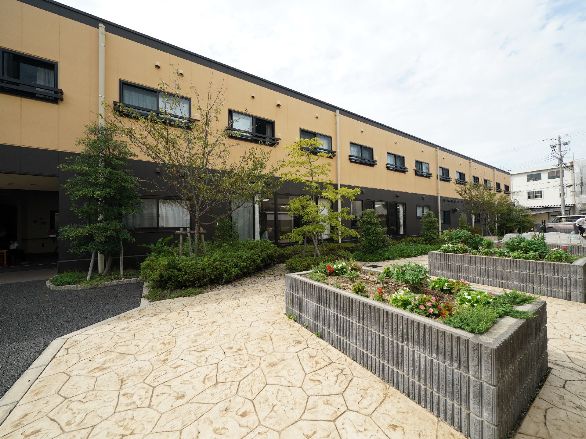 二階建ての建物と、その手前の石畳と手入れされた植栽や花壇