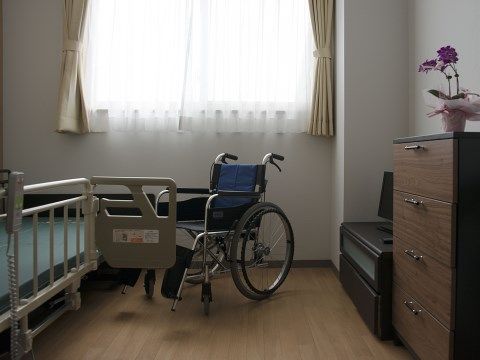 居室の壁際にはタンスとテレビが、反対側には介護用ベッドが配置されている。また中央には車椅子が配置されている。