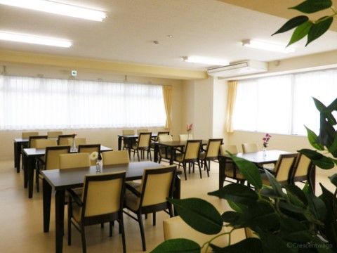 観葉植物が飾られ、窓からの光と蛍光灯で明るく照らされた広々とした空間である。６セットのテーブルや椅子が並べられている。