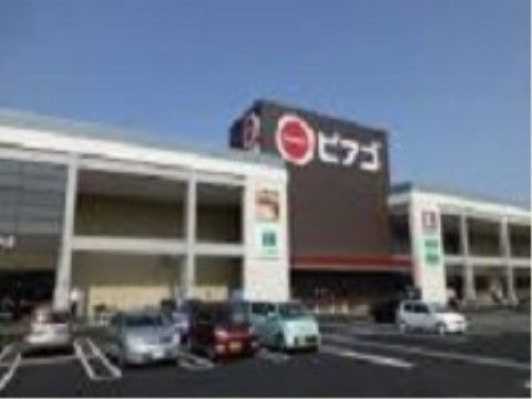 大きな建物の手前に数台の車が停められた青空駐車場がある。建物にスーパーマーケットのマークと名前が表示されている。