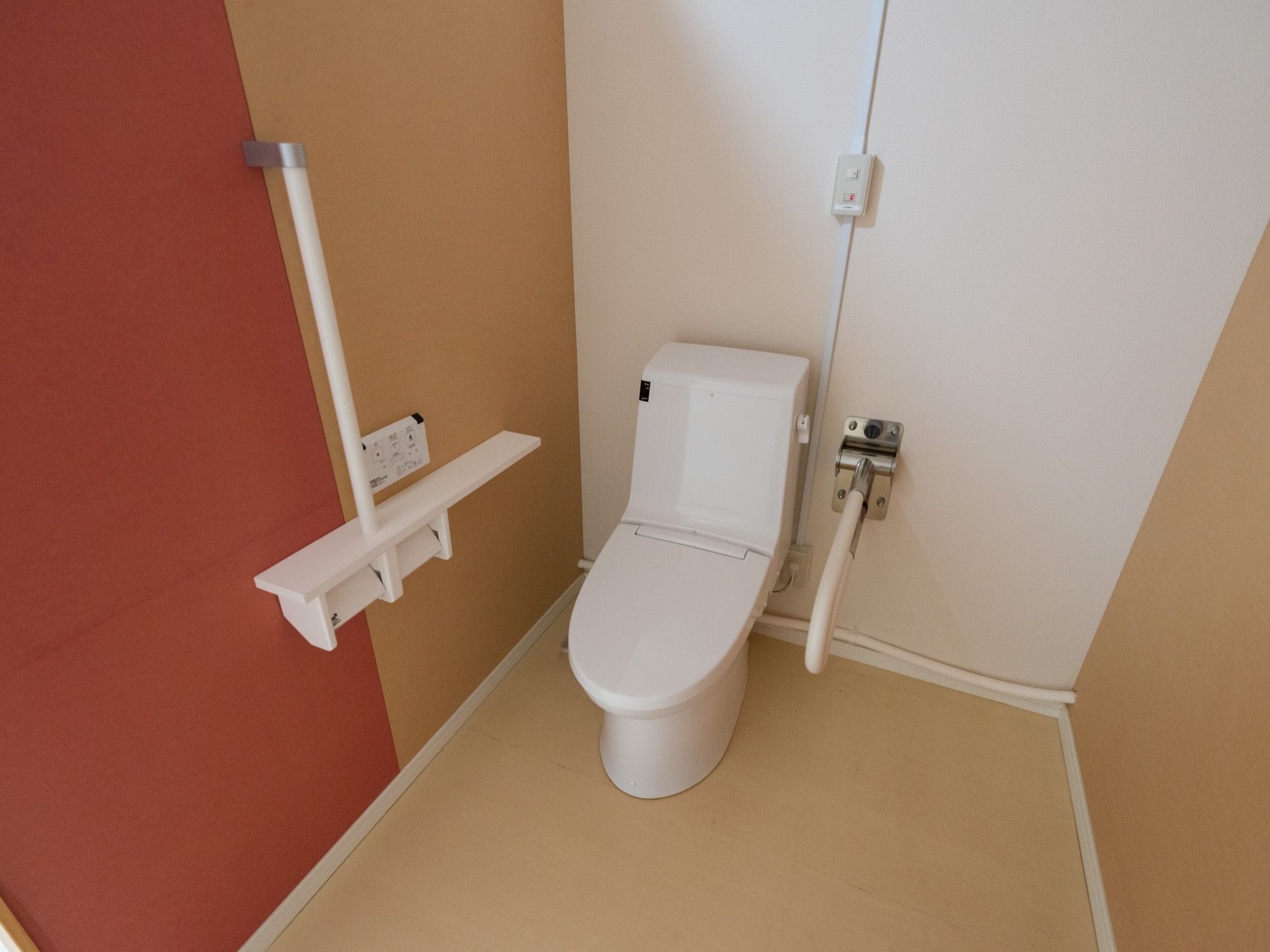 トイレにふたつきの便器が設置されている。トイレットペーパーホルダーが２つ並んでいて、その上に便座の操作パネルがある。