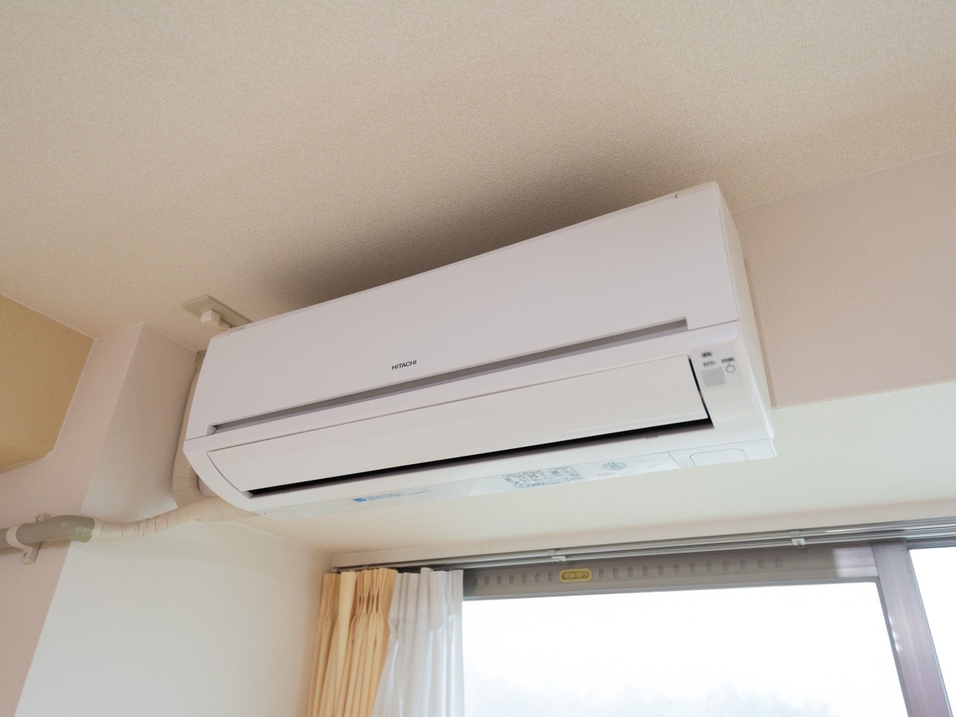 居室の窓の上の壁にエアコンを設置。左側に伸びている電源コードや配管は化粧カバーやテープで覆われている。