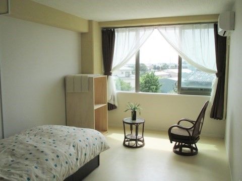 ベッド、小さなテーブル、椅子と棚が置かれているシンプルな部屋