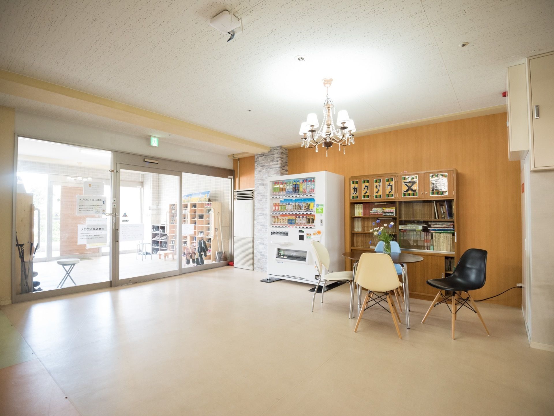 クリーム色の床の広い空間にガラスの自動扉から光が差し込んでいる。壁際に本棚と自動販売機が設置されている。