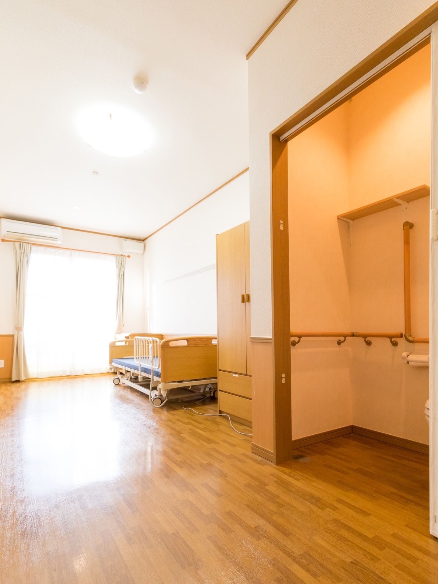 手前にトイレがあり、手すりが見える。奥にはベッドとクローゼットが置かれている。広いスペースのある居室である。