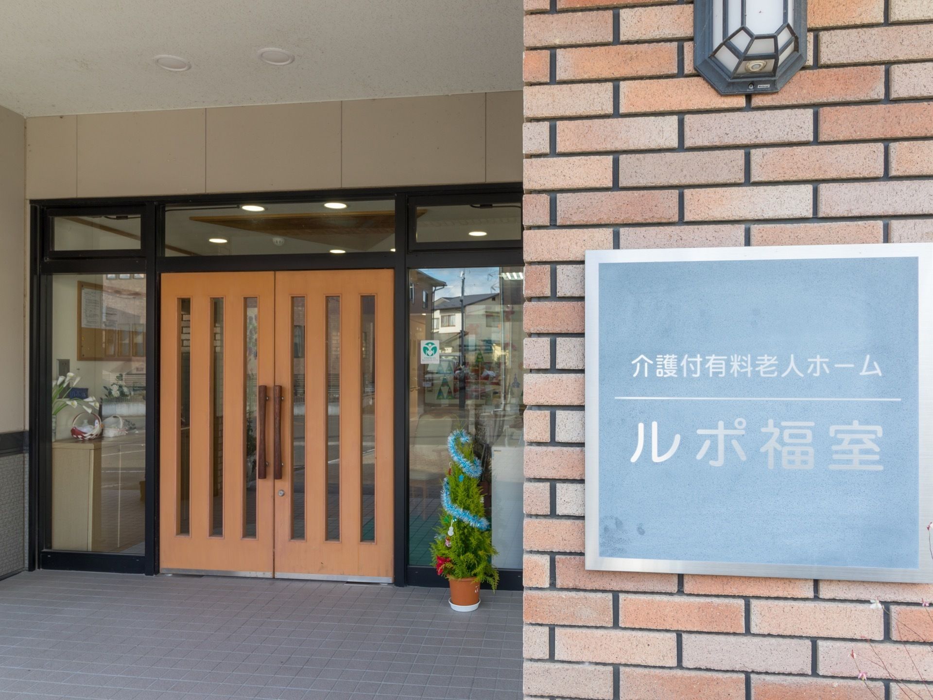 玄関の右側のレンガの壁には施設名の表札を設置している。緑色にグレーの文字で書かれ、読みやすくなっている。