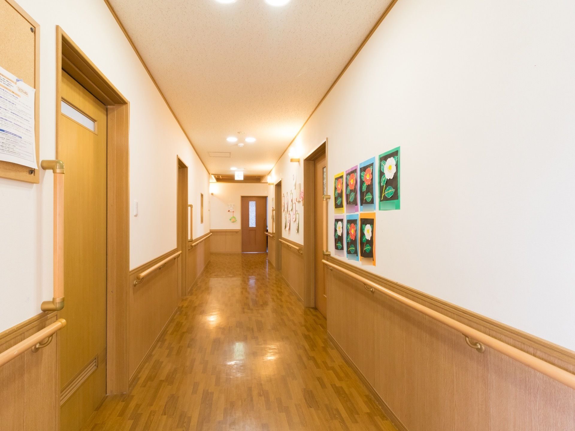 明るく広々とした廊下になっている。入居者様のお花の作品が飾られ、明るい雰囲気になっている。壁には手すりが設置され安全である。