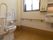 深みのある木目調の床のトイレスペースである。便器の正面には窓があり、その横側に洗面台を取り付けている。傍には、ハンドペーパーを備えている。