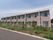 薄い紫の外壁と白い柱でできた２階建ての建物である。周囲は植栽とフェンスで囲まれている。居室の窓が並んでいる。