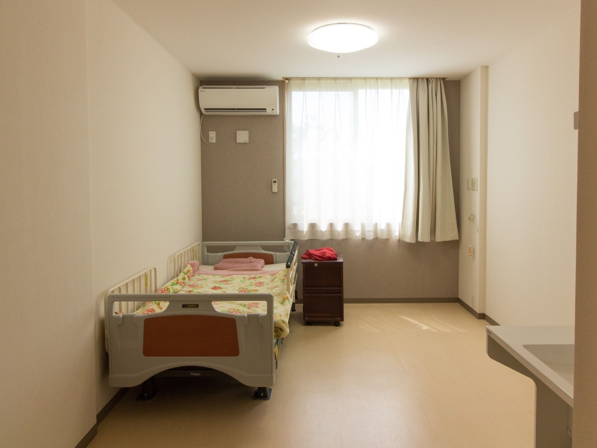 天井、壁、床ともに白で統一された部屋である。壁際にベッドが置かれている。窓にはカーテンが取りつけられ、窓横にエアコンが設置されている。