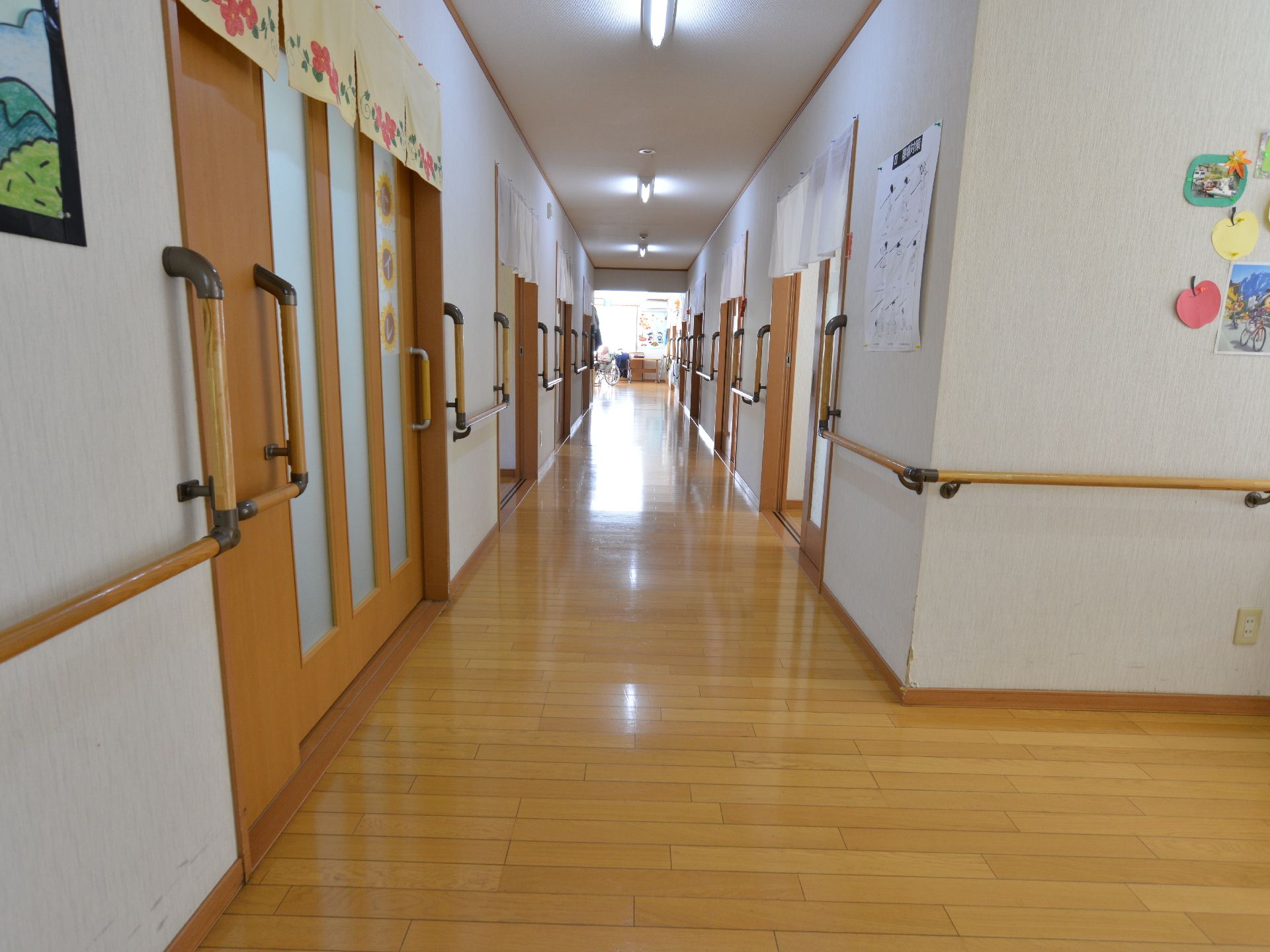 廊下は、木目調の床で段差がなく安心して通行出来る。壁には、手すりがあるので、安全に配慮されたつくりとなっている。