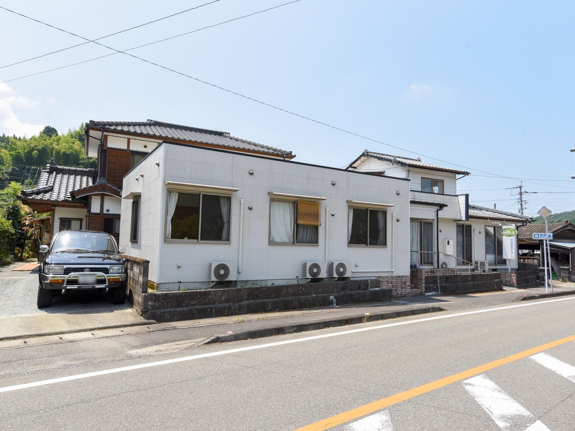 豊富な自然と隣り合った住宅地に、施設の建物も溶け込んでいる。敷地は道路に面しており、建物の横に車が駐車されている。