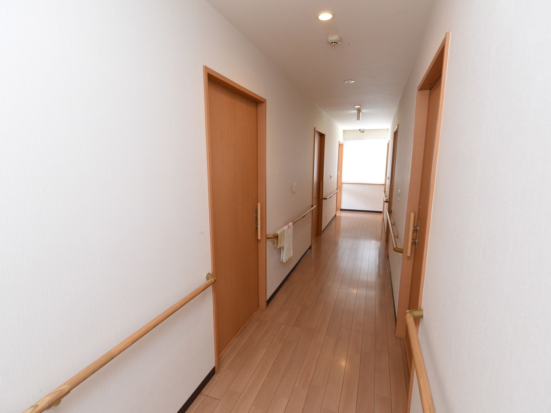 通路の壁には、丈夫そうな手すりがしっかり取りつけられている。白い壁に、各部屋に入る扉が均等に並んでいる。